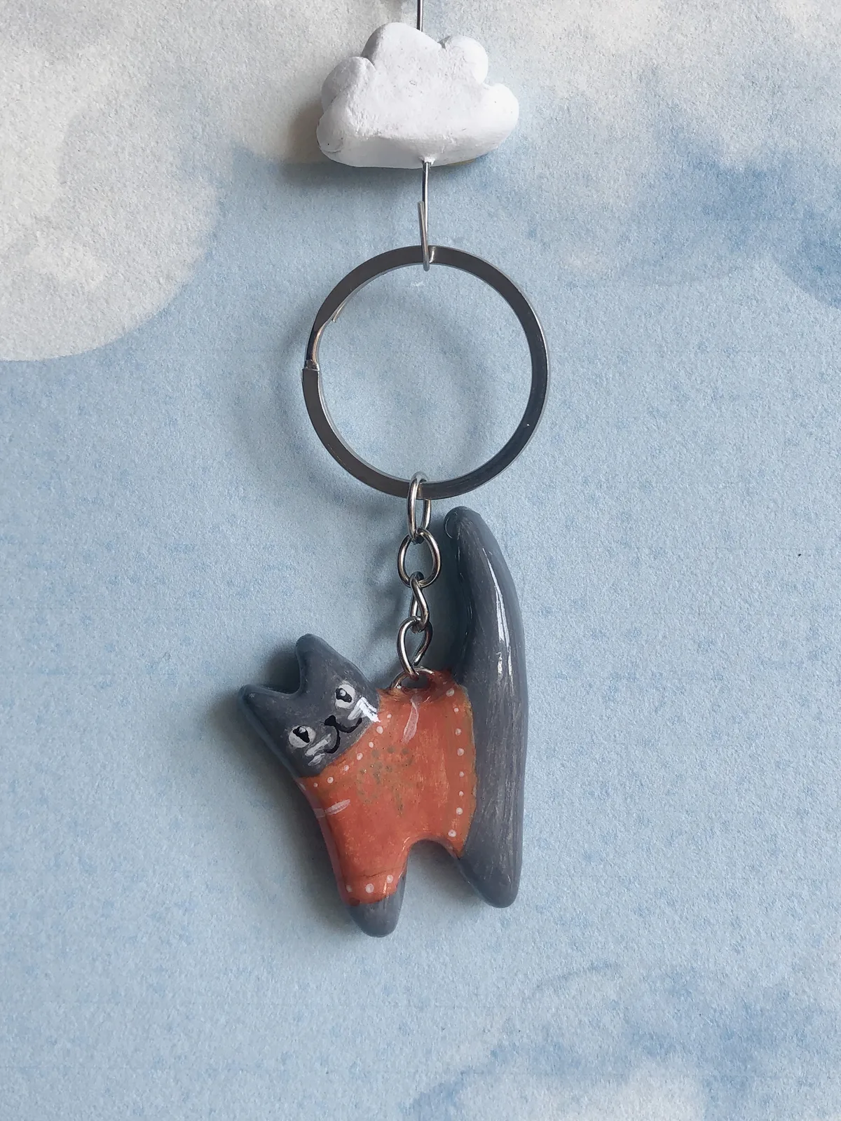 Llavero de gatito atigrado con sweater rojo frente a un cielo con nubes