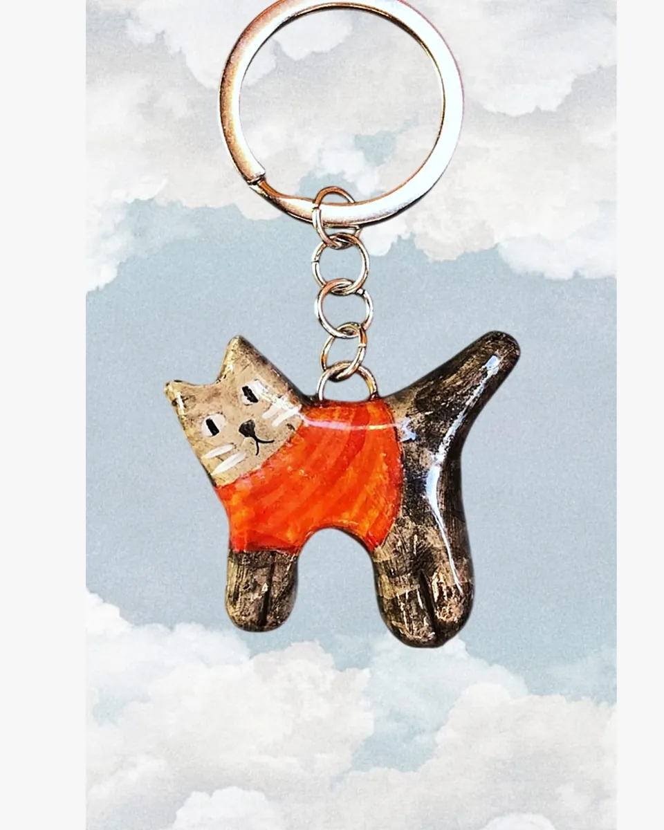Llavero de gatito atigrado con sweater rojo frente a un cielo con nubes