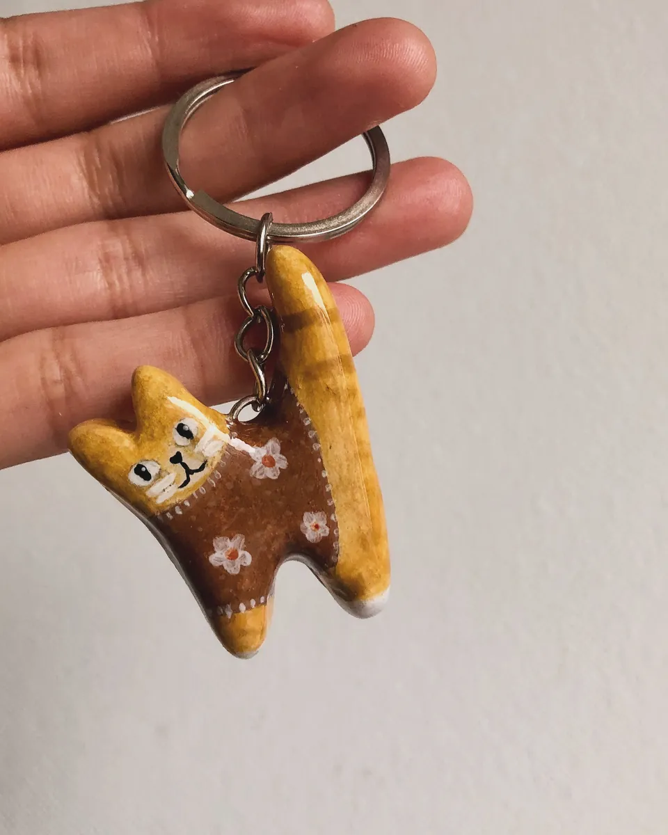 Llavero de gatito naranjo con sweater café de flores, en la mano