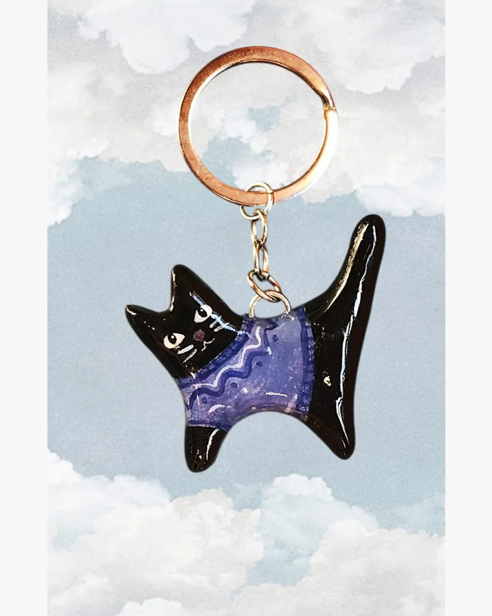 Llavero de gatito negro con sweater morado frente a un cielo con nubes