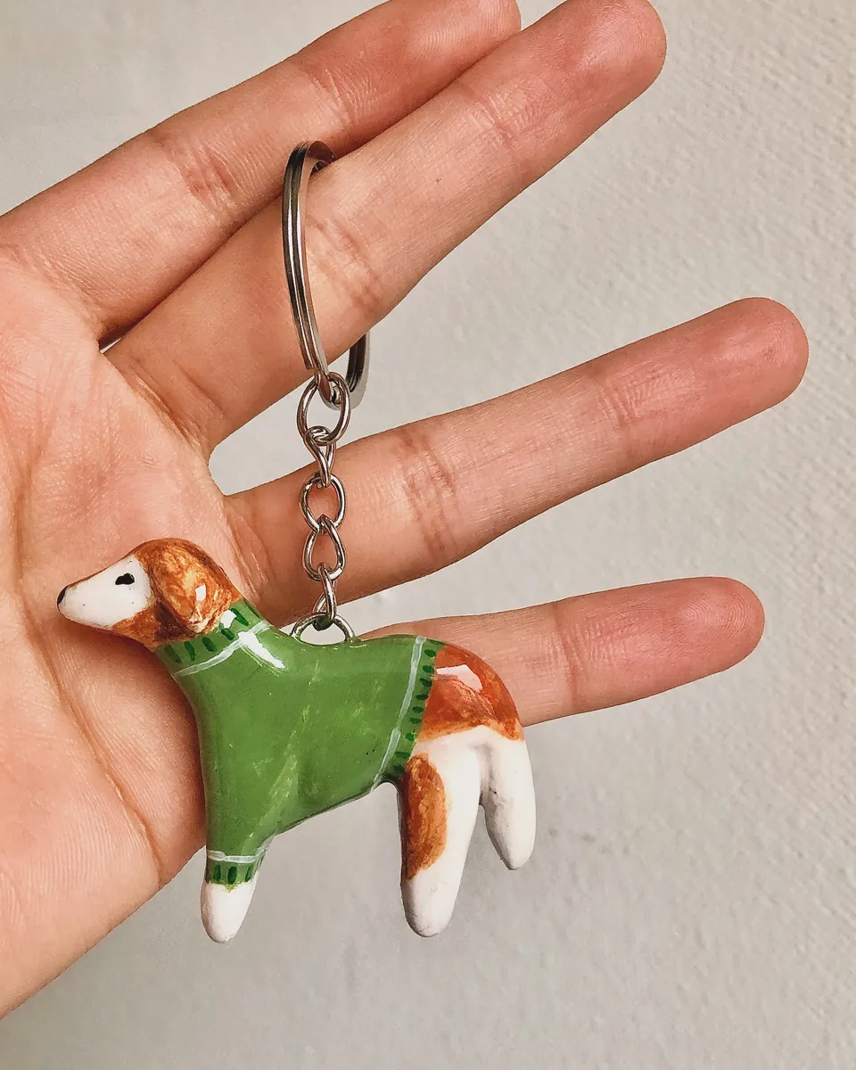 Llavero de perrito café y blanco con sweater verde, en la palma de una mano